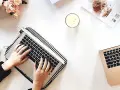 Kobieta pisze na laptopie, przygotowując wypowiedzenie umowy o dzieło. Obok świeca, muffinka i bukiet kwiatów.