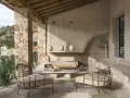 Acogedora terraza interior piso con sillones de metal, sofá y mesa de centro de piedra, bajo un techo de madera y rodeada de muros de piedra.