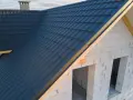 Nowy dach z ciemnogranatowej blachodachówki, wiatrownica zamontowana. Trwa obróbka dachu.