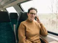 Kobieta w brązowym swetrze rozmawia przez telefon w pociągu. Czas na moją kolej, by usiąść przy oknie i podziwiać widoki.