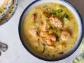 Sopa cremosa de pescado con salmón, gambas y mejillones, decorada con perejil.