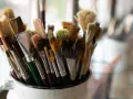 Gros plan sur un pot rempli de pinceaux de peinture aux poils variés, certains neufs, d'autres usagés.