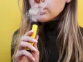 Mujer exhala vapor de un vaper sin nicotina, pero ¿sabías que el vaper sin nicotina mancha los dientes?