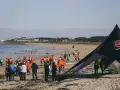 Rassemblés sur la plage pour une course de longe côte, des participants en tenues colorées attendent le départ sous un ciel clair.