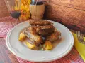 Succulente costine di maiale in padella, dorate e saporite, servite con patate arrosto e un rametto di salvia.