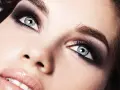 Occhi azzurri intensificati da un trucco smokey eyes audace, con labbra lucide e un accenno di sorriso.