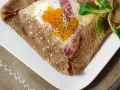 Une galette bretonne garnie d'un œuf, de jambon et de fromage, poivrée et décorée d'une feuille verte. Un délice de french crepes !