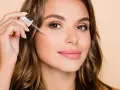 Kobieta aplikuje serum z pipetką na policzek. Dowiedz się, jak stosować retinol dla pięknej cery.