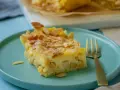 Ein Stück schneller Apfelkuchen mit Schmand und Pudding, bestreut mit Mandelblättchen und Zimt, auf einem türkisfarbenen Teller.
