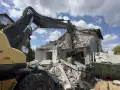 Koparka Volvo niszczy budynek. Trwa rozbiórka budynku, cena za m2 jest kluczowa przy planowaniu prac.
