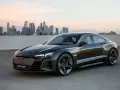 Ciemnoszary Audi e-tron GT stoi na tle panoramy miasta o zachodzie słońca.