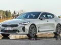 Elegancka Kia Stinger 2025 w kolorze srebrnym, zaparkowana na mokrej nawierzchni, z drzewami w tle.