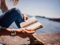 Persona sentada junto al agua, leyendo un libro en francés.