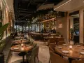 Elegantes mesas y un bar iluminado, con arte mural y plantas, ofrecen **ideas decoración restaurante** acogedoras.