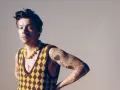 Harry Styles w kamizelce w romby i żółtym naszyjniku, jakby inspirował nowe harry styles utwory.