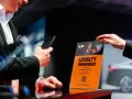 Ein Mann hält ein Smartphone, während eine Hand ein orangefarbenes Schild mit der Aufschrift "Loyalty Rewarded" und dem SIXT ONE Logo hochhält.