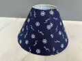 Un abat-jour conique bleu marine orné de motifs d'ancre et de roue de gouvernail. Idéal pour fabriquer un abat-jour en tissu plissé avec une touche marine.