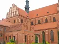 Potężny zamek krzyżacki w Pelplinie, z cegły i czerwonym dachem, góruje nad okolicą.