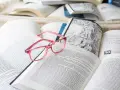 Różowe okulary spoczywają na otwartych książkach, tworząc atmosferę nauki i wiedzy. ibidem.