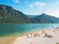 Spiaggia affollata sui laghi in Piemonte, ideale per una gita in moto. Montagne verdi e acqua azzurra.