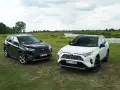 Dwa SUV-y: ciemny i biały Toyota RAV4 hybryda, stoją na łące nad jeziorem.