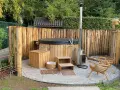 Entspannende gartendusche ideen: Ein Whirlpool mit Holzverkleidung, daneben ein Holzofen und Sitzgelegenheiten aus Holz.