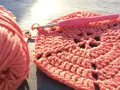 Koralowa włóczka i szydełko tworzą wzór. Widać tu piękne oznaczenia szydełkowe, które tworzą ażurowy efekt.