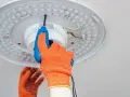 Ręka w pomarańczowej rękawicy odkręca śrubę plafonu LED. Instrukcja jak zdjąć plafon krok po kroku.