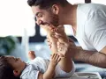 Ein lachender Vater mit Kind spielt liebevoll mit den Füßen seines Babys.