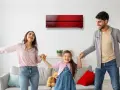 Familia feliz bailando en una sala con aire acondicionado inverter rojo. Disfrutan del confort y bajo consumo kwh.