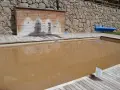 Piscina de sal con agua turbia y rodeada de madera. Al fondo, una pared de piedra y duchas.