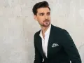 Elegancki mężczyzna w ciemnozielonej marynarce i białej koszuli z ozdobną poszetką. Jego kołnierzyk koszuli, czyli stójka, jest lekko rozpięty.