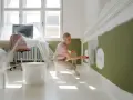 Kobieta maluje ścianę na zielono, klęcząc obok wiadra z farbą.
