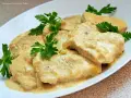 Filet z indyka w sosie śmietanowym, udekorowany natką pietruszki, prezentuje się apetycznie na białym talerzu.