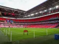 Pusta, czerwona trybuna stadionu Wembley, największego stadionu na świecie, z zieloną murawą i tabliczką "Prosimy nie wchodzić na trawę".