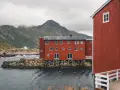 Czerwone domy rybackie nad wodą, w tle góry. Czy lecąc do Norwegii potrzebny jest paszport? Tak, jeśli nie jesteś obywatelem UE/Schengen.