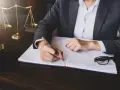 Prawnik sporządza przykładowe uzasadnienie wniosku o upadłość konsumencką. Na biurku waga sprawiedliwości i młotek sędziowski.