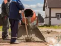 Dwóch budowlańców miesza beton w betoniarce. Widać, ile żwiru na worek cementu potrzeba do uzyskania odpowiedniej konsystencji.