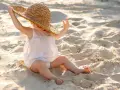 Liten bebis med stråhatt på stranden, njuter av solens värme.