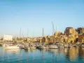 Port w Heraklionie na Krecie, pełen żaglówek i jachtów, z zabytkowymi budynkami w tle.