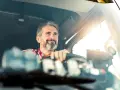 Uśmiechnięty kierowca ciężarówki, po przejściu kwalifikacji wstępnej, zapatrzony w dal.