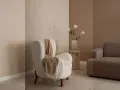 Gemütliches Wohnzimmer mit beigen und braunen Wandfarben. Ein flauschiger Sessel mit Decke und ein Sofa laden zum Entspannen ein.