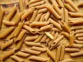 Makaron pełnoziarnisty vs zwykły: penne w odcieniach brązu i żółci, ułożone na drewnianym tle.
