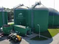 Zielone zbiorniki instalacji biogazowej, z logo "DYNAMIC BIOGAS MADE IN POLAND". Obok ładowarka i kontener.