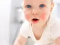 Niemowlę z zaczerwienioną wysypką na twarzy, niebieskimi oczami i otwartymi ustami.