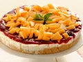 Deliziosa cheesecake al melone, con topping di frutta fresca e salsa rossa, su un piatto bianco.