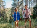 Coppia sorridente fa nordic walking tra gli alberi, godendosi i benefici di questa attività all'aria aperta.