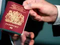 Dłoń podaje paszport biometryczny Wielkiej Brytanii. Widoczny herb i napis "PASSPORT".