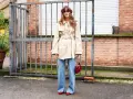 Mujer con gabardina beige y vaqueros bootcut, gafas rojas y bolso rojo.