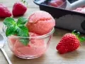 Erfrischendes Erdbeer-Sorbet-Eis in einer Glasschale, garniert mit Minze. Daneben liegen frische Erdbeeren.